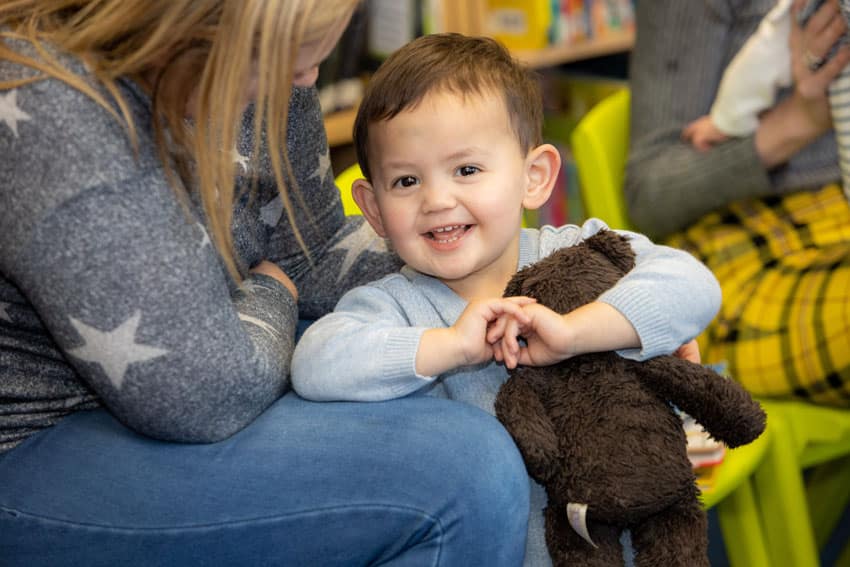 A happy young boy holding a tedding bear with his mother at an Aura Wales Library