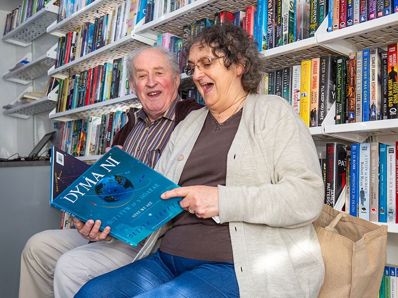 A happy senior couple reading a Welsh book at an Aura Wales Library
